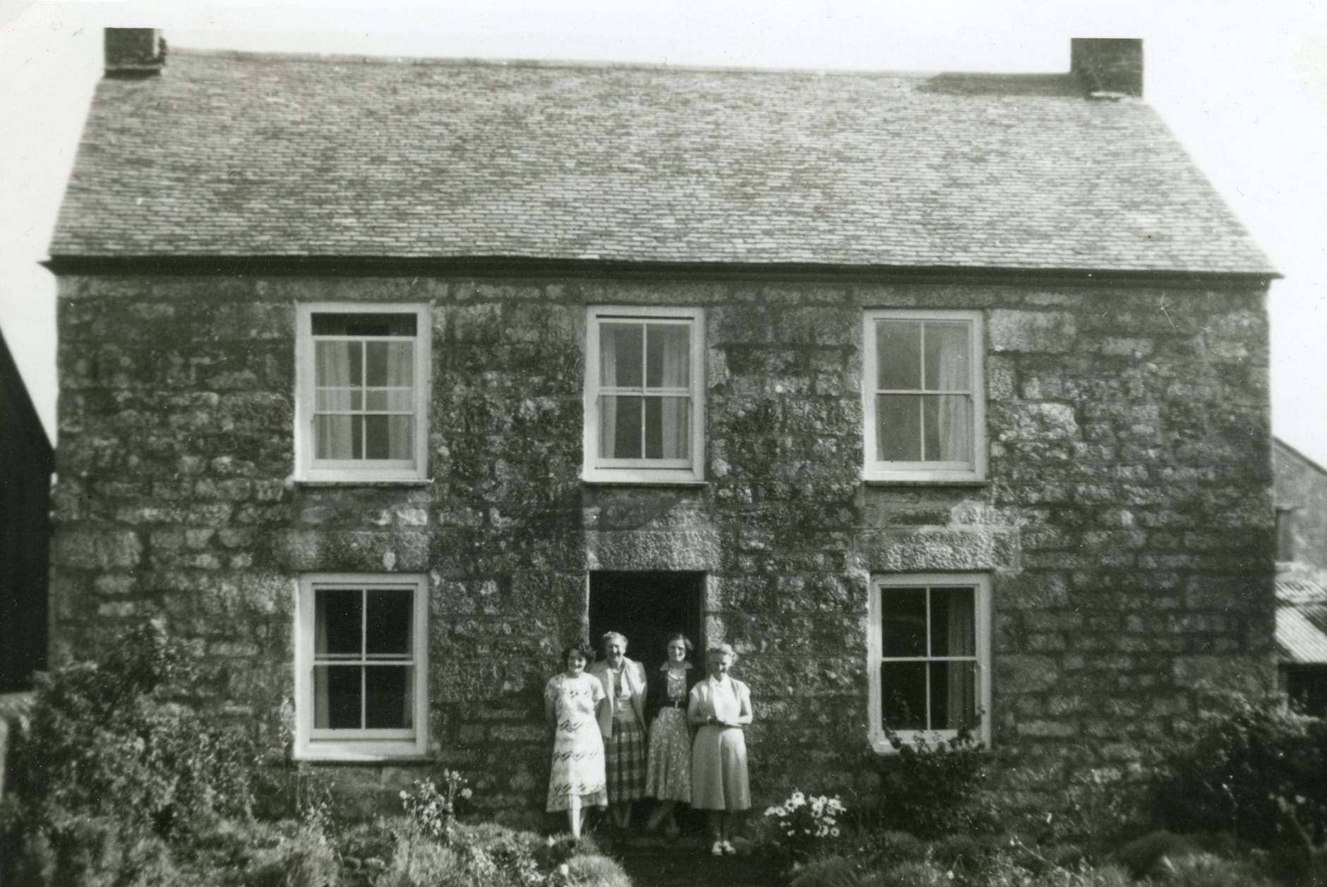 grayscale photo of four women standing in front of house
